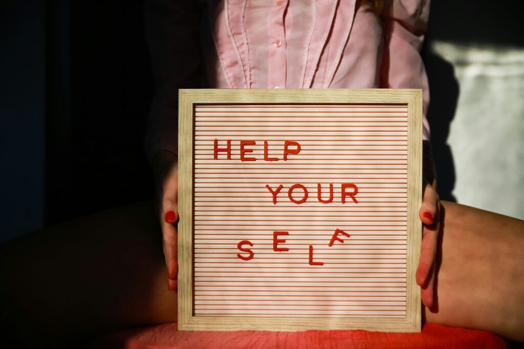 Hands holding a small push-pin boards, with letters spelling out "Help Your Self"